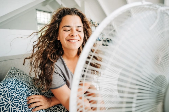 Person kühlt sich mit einem Ventilator auf dem Sofa ab.